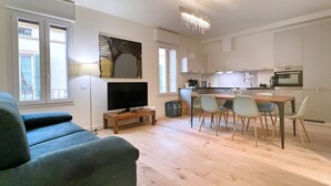 A modern living room with a flat-screen TV, a sofa, and a dining area with chairs and a table. - UR-NEST San Giorgio - gorgeous flat (Bologna)