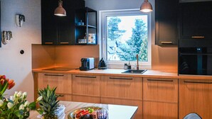 A modern kitchen with wooden cabinets, a window with a view of trees, a coffee maker, and a fruit bowl on the counter. - Awesome apartment in Stezyca with sauna (Stezyca)