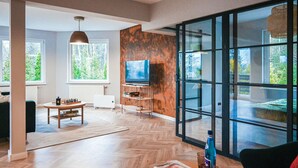 A modern living room with a large TV, wooden flooring, and a view through large windows. - Awesome apartment in Stezyca with sauna (Stezyca)