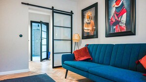 A modern living room with a blue sofa, a sliding glass door leading to another room, and two framed artworks on the wall. - Awesome apartment in Stezyca with sauna (Stezyca)
