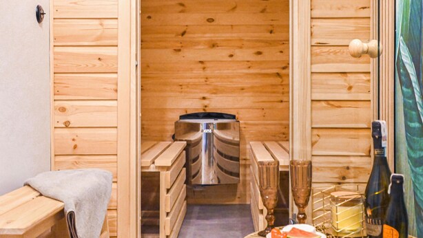 A sauna room with wooden benches and a sauna head. There is a bottle of wine and a glass on a small table. - Awesome apartment in Stezyca with sauna (Stezyca)