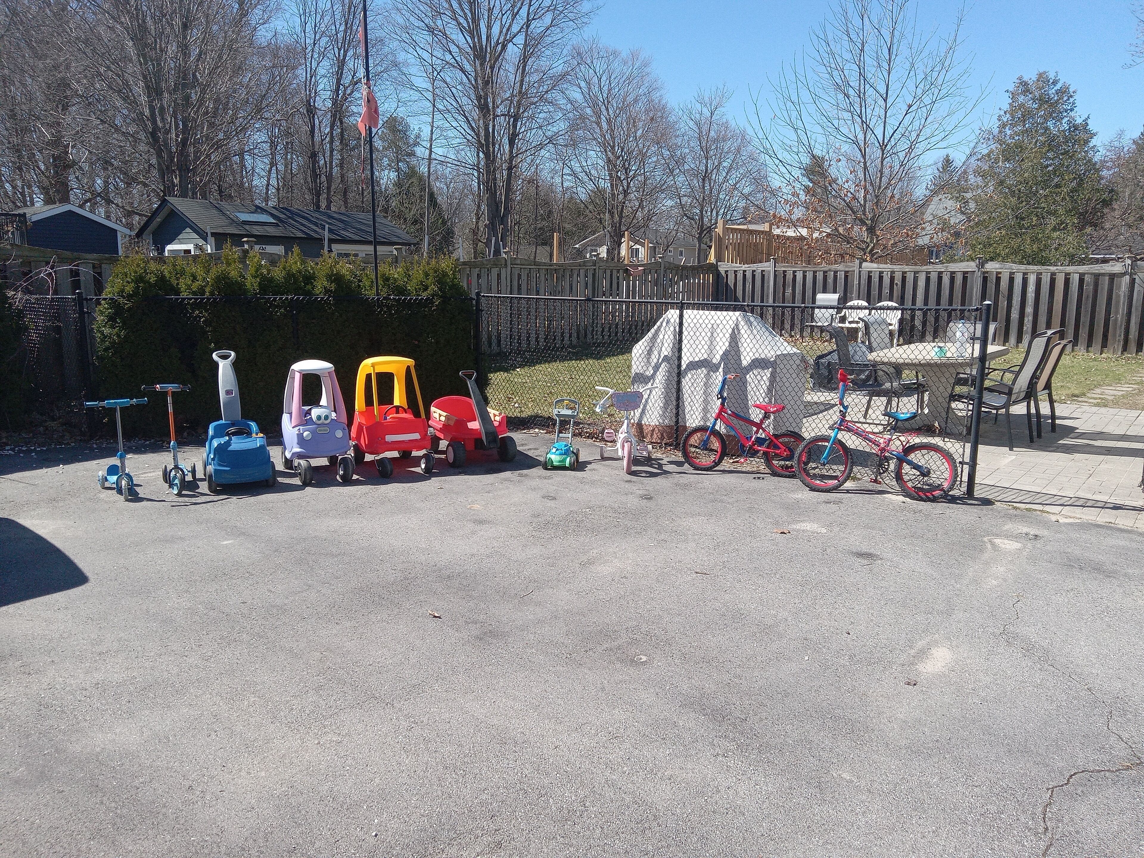 Ein Parkplatz mit verschiedenen Spielsachen und Fahrzeugen für Kinder, darunter Spielzeugautos, ein Roller und ein Fahrrad.