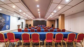 A conference room with a long table, red chairs, and a stage at the front.