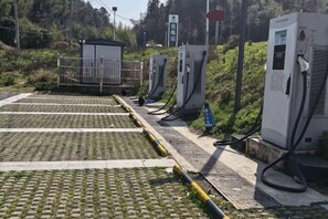 Een parkeerplaats met laadpalen voor elektrische voertuigen, een klein dak en een verhard oppervlak.