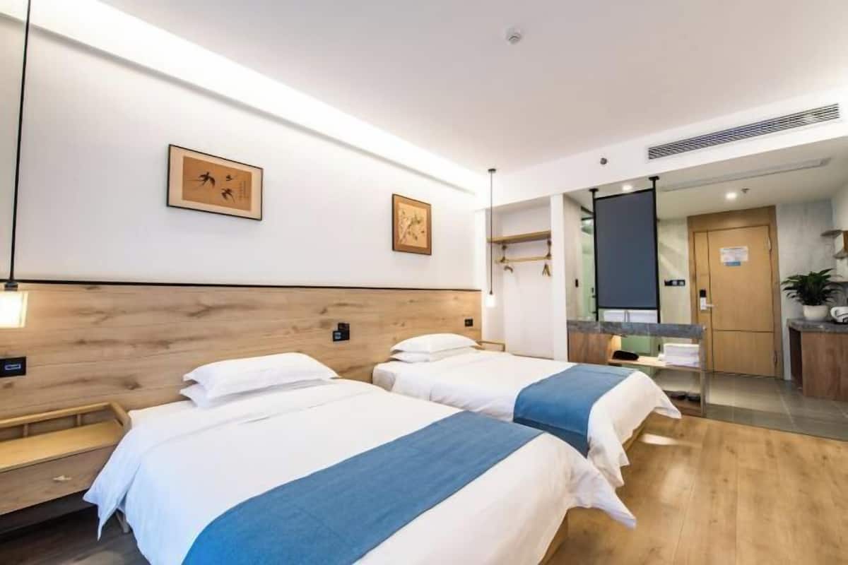 Habitación de hotel con dos camas, cabecera de madera, un escritorio pequeño y un espejo.