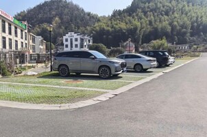 En parkeringsplats med flera bilar, en byggnad med en skylt och en kuperad bakgrund.