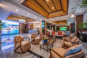 Un hall de hotel con asientos de cuero, un mostrador de recepción y una gran pantalla de televisión.