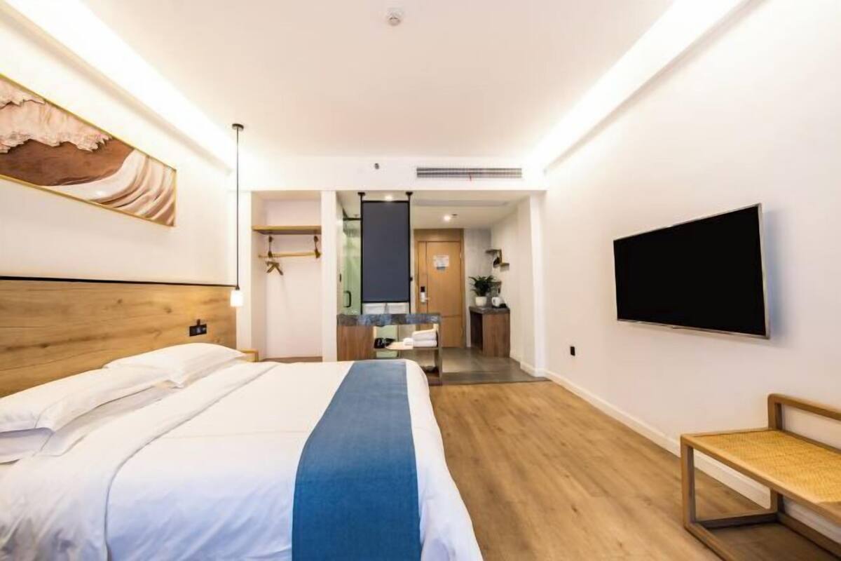 Habitación de hotel con cama, televisión, banca y puerta que da a un baño.