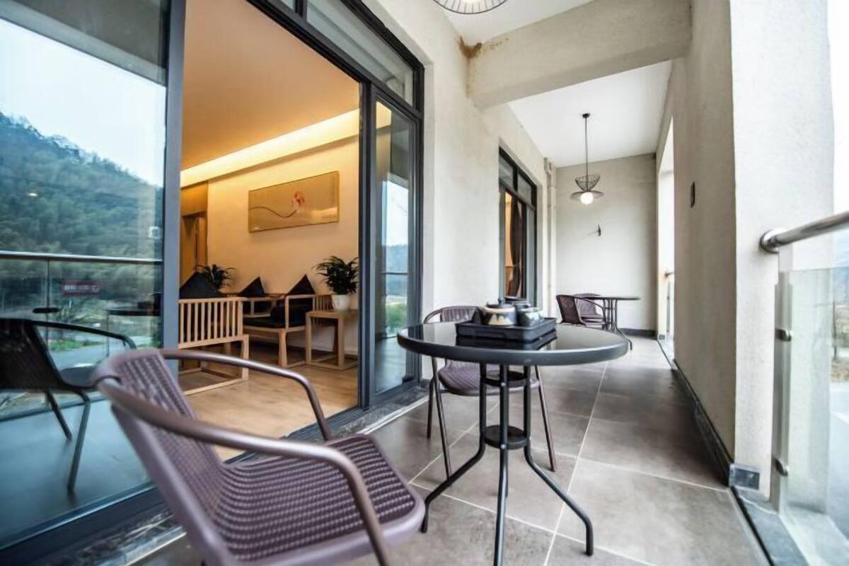Un balcón con una mesa y sillas, una puerta de cristal que da a una habitación interior y vistas al exterior.