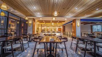 A spacious dining area with a long table and multiple chairs, a bar area with stools, and a modern ceiling design.