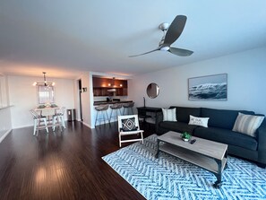 Uma sala de estar moderna com piso de madeira escura, um sofá cinza, uma mesa de centro e um ventilador de teto.
