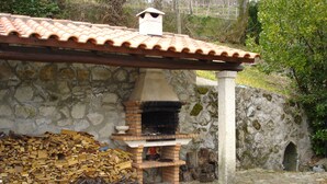 Un edificio de piedra con tejado de tejas, un horno de ladrillo y una pila de leña.
