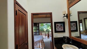 Une salle de bain avec une porte en bois, un grand miroir, un lavabo et un tableau encadré au mur.