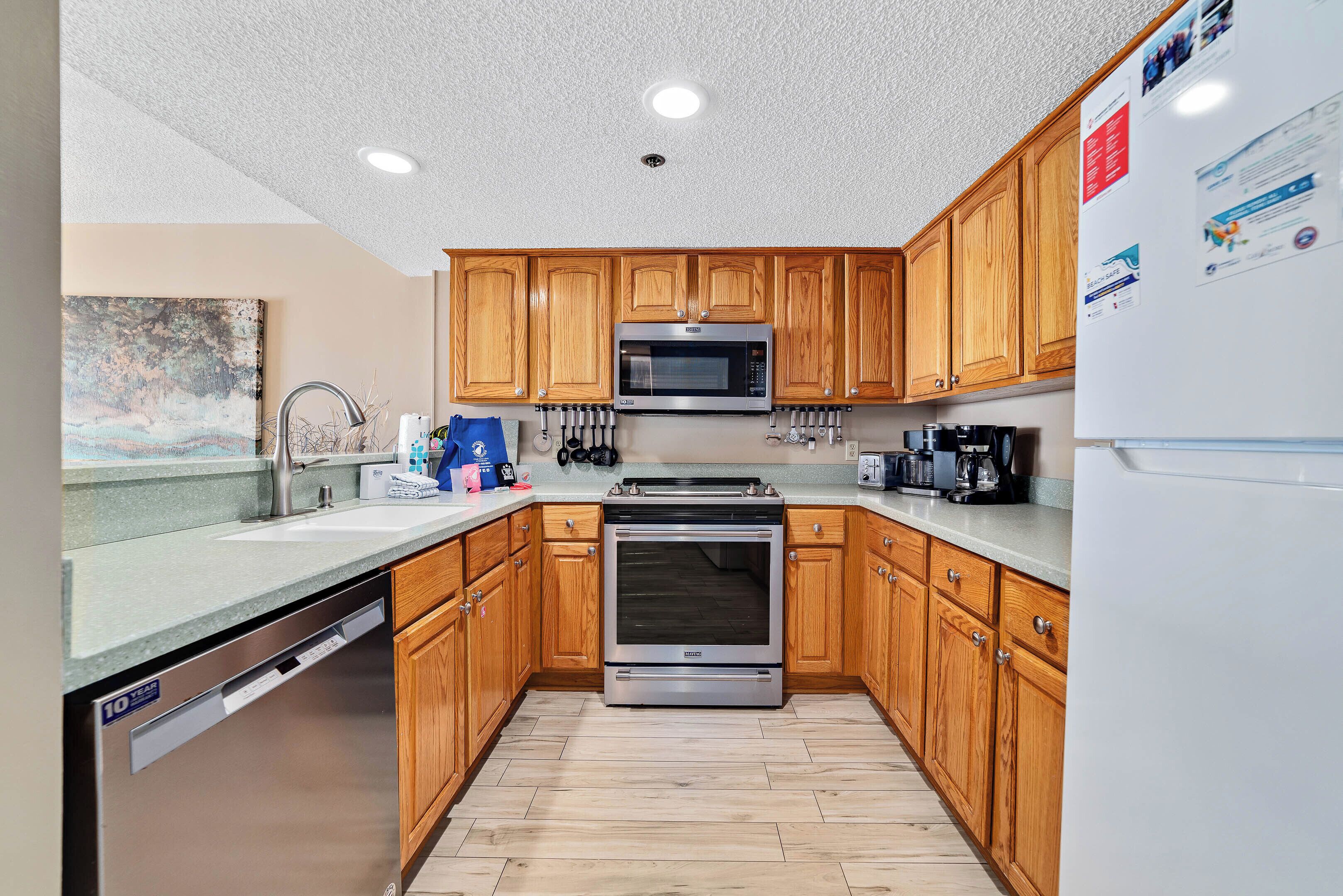 A compact kitchen with wooden cabinets, a stainless steel dishwasher, a built-in oven, and a microwave.