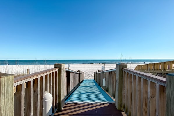 A wooden boardwalk leading to a beach with a clear blue sky.
