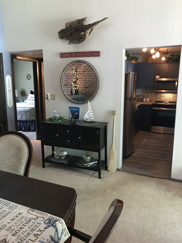 Un comedor con una mesa, sillas, una consola negra con objetos decorativos, un espejo y un letrero sobre la consola.