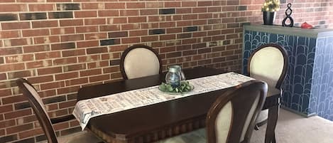 A dining table with four chairs, a decorative table runner, a small potted plant, and a candle holder.
