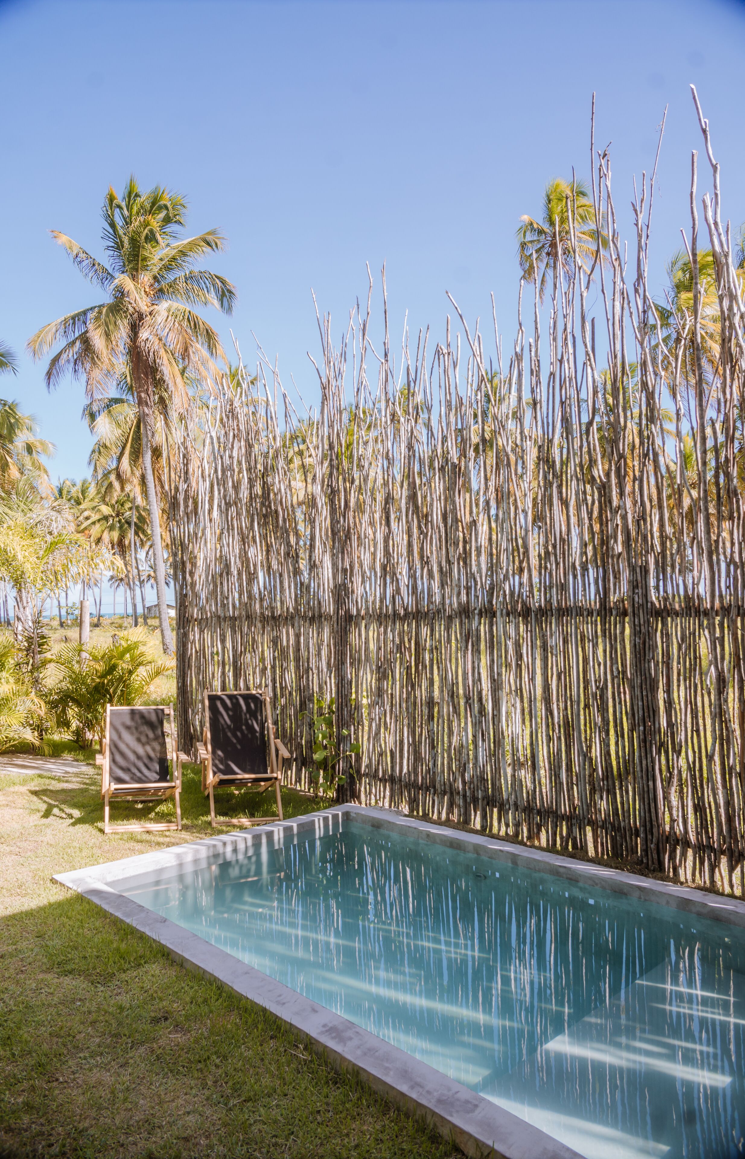 A rectangular pool with clear water, surrounded by a bamboo fence, and two wooden chairs.
