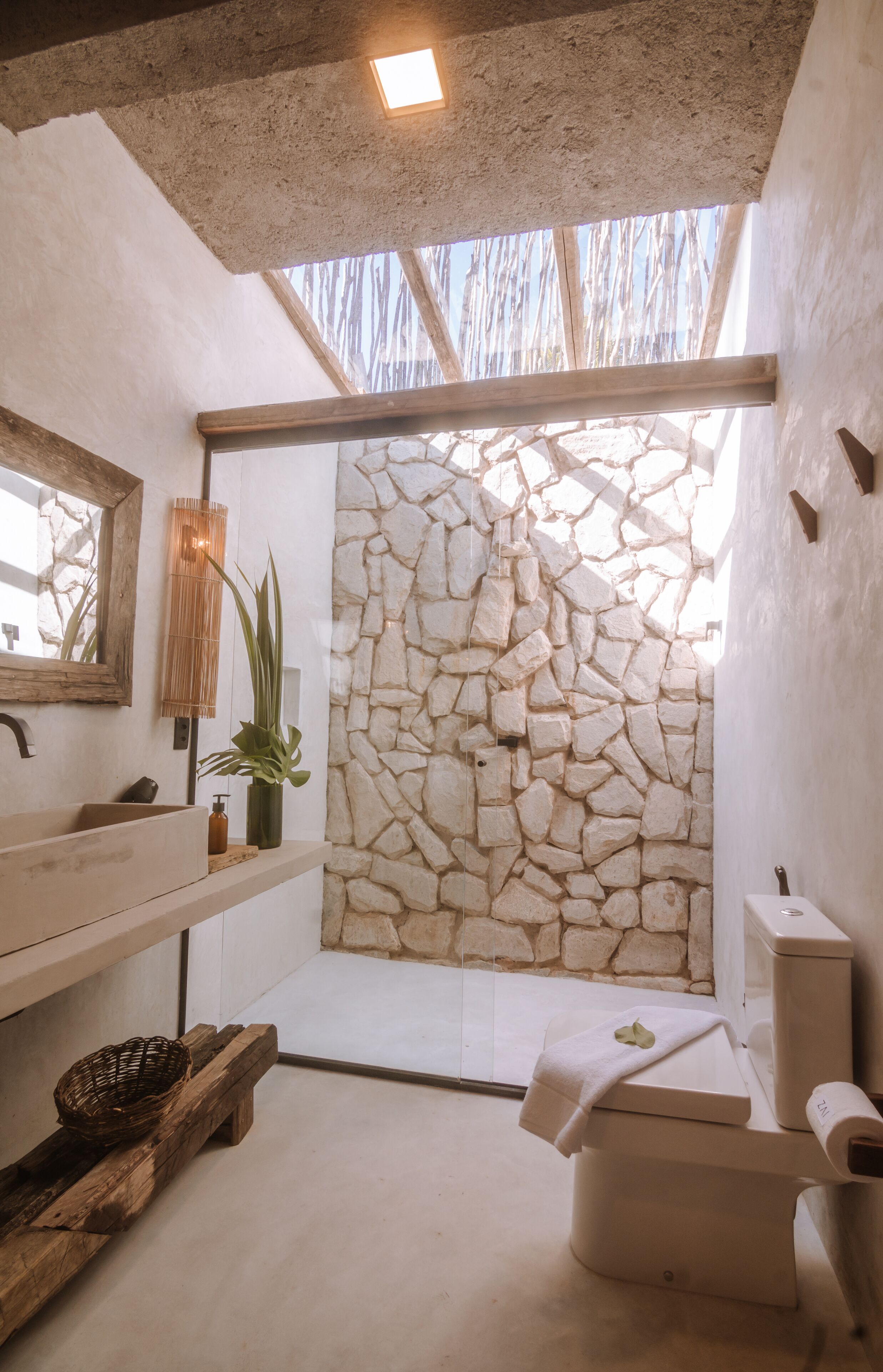 Un baño con pared de piedra, banca de madera, lavamanos y retrete.