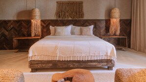 A bedroom with a large bed, wooden headboard, two nightstands, woven lamps, and a small wooden table. - Zai Patacho (Porto de Pedras)