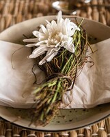 A bouquet of white flowers with green stems and leaves, placed on a white plate with a textured surface.