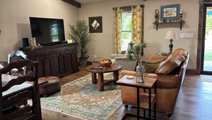 A cozy living room with a television, wooden furniture, a large plant, and a window with curtains. - Secluded 2 Bedroom Sanctuary on 20 Acres in the Heart of the Bourbon Trail (Chaplin)