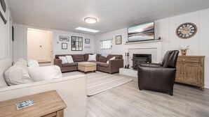 Een woonkamer met een hoekbank, een lederen fauteuil, een open haard en een televisie.