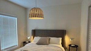 Una cama bien tendida con sábanas blancas y dos toallas dobladas, un cabecero oscuro y dos lámparas de noche sobre mesitas a juego.