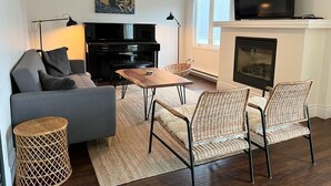 Una sala de estar con un sofá, una mesa de centro, sillas de mimbre, una chimenea, un televisor y un cuadro en la pared.