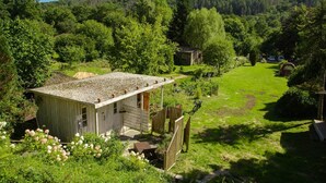 Una cabaña rústica con techo de grava, rodeada de exuberante vegetación y un paisaje montañoso.
