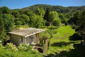 Una cabaña rústica con techo de grava, rodeada de exuberante vegetación y un paisaje montañoso.