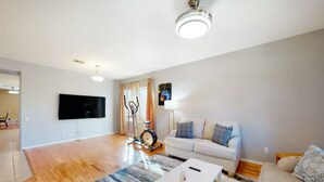 Un salon spacieux équipé d’un téléviseur à écran plat, d’un vélo d’appartement, d’un canapé blanc et d’une table basse.