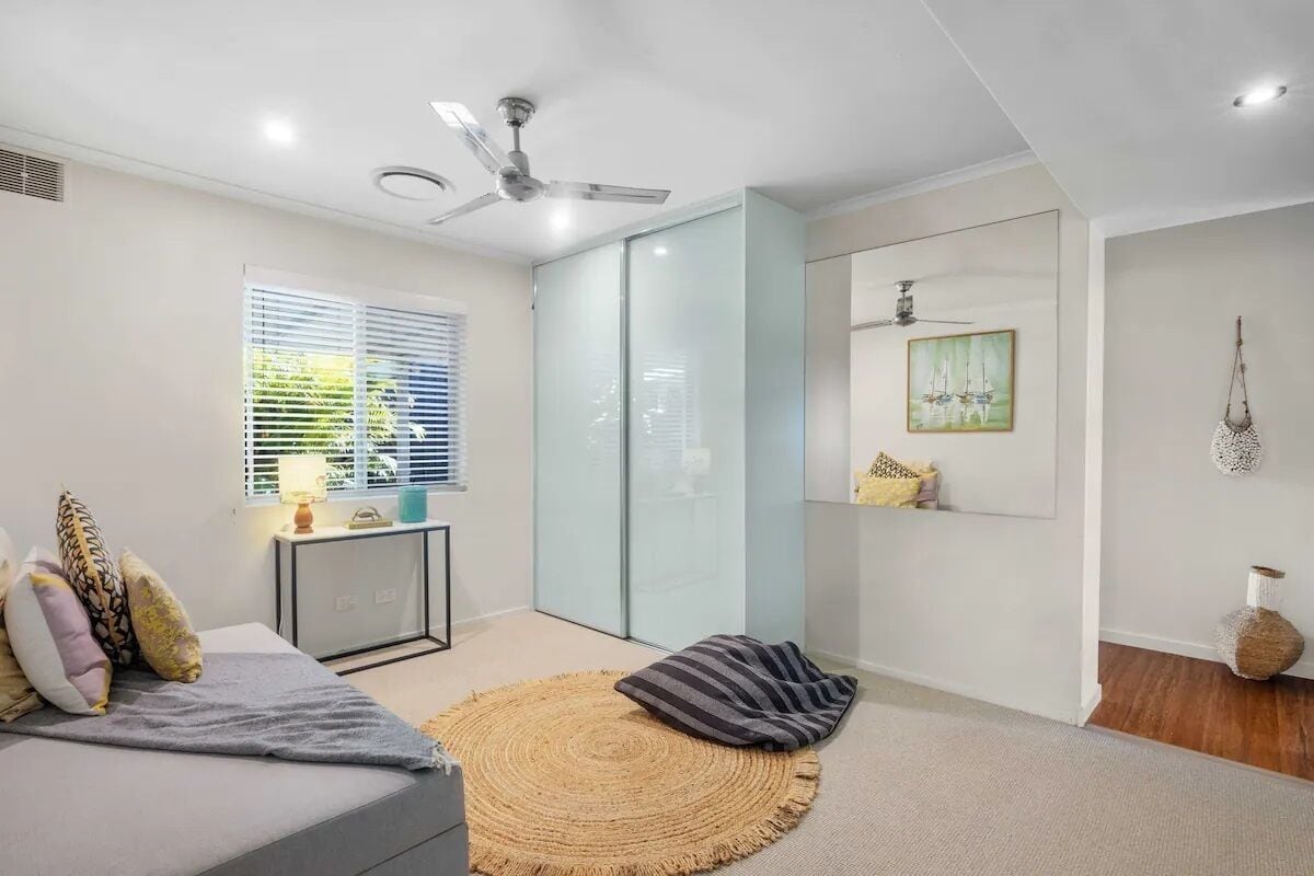 Een moderne slaapkamer met een bed, een nachtkastje, een lamp, een plafondventilator en een groot raam met jaloezieën.