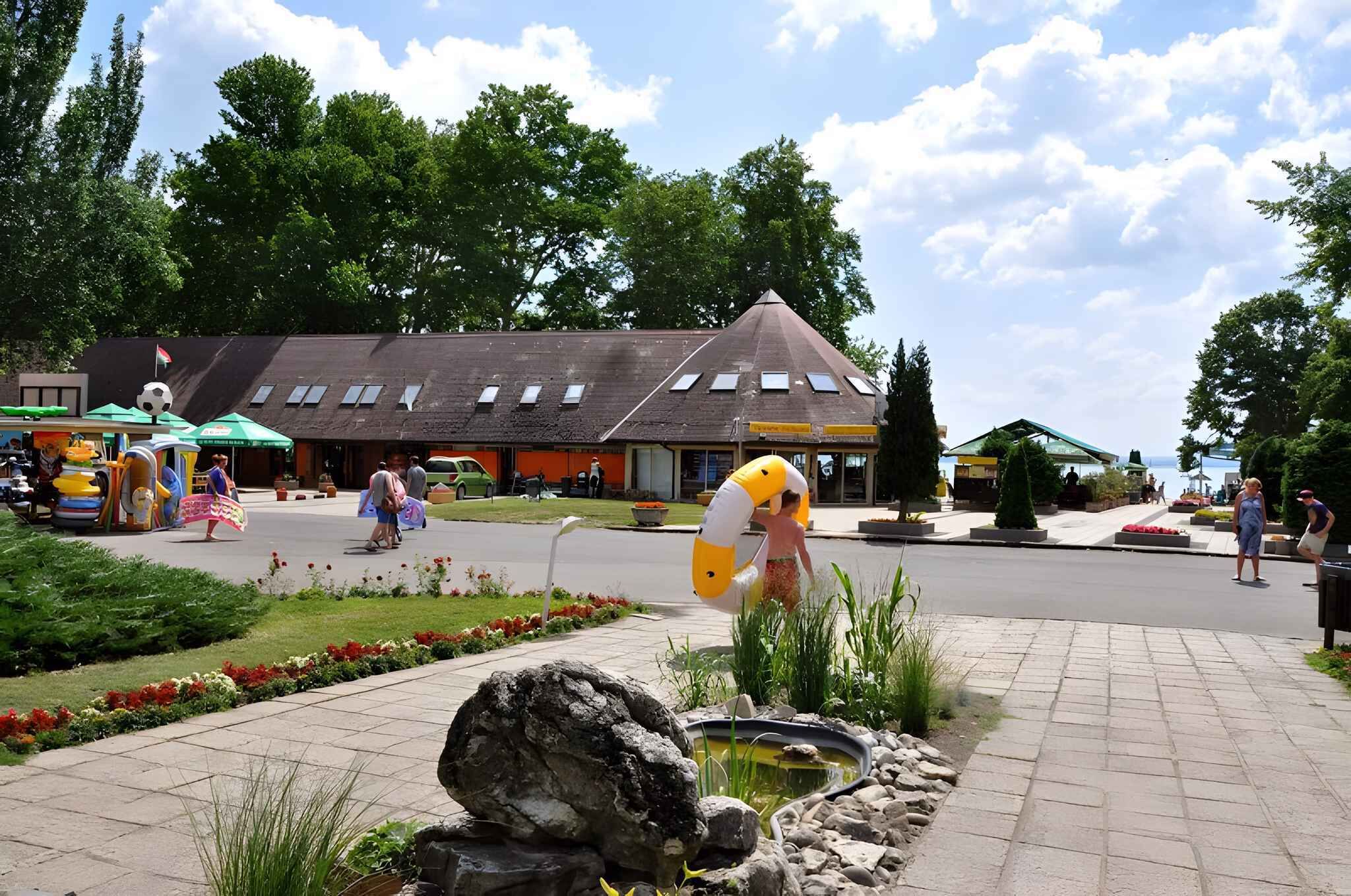 Una piazza pubblica con uno stagno, panchine e un edificio con tetto spiovente.