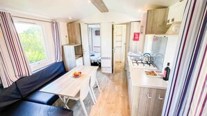 Een compacte kitchenette met een gasfornuis, spoelbak en een klein eethoekje met een tafel en bank.