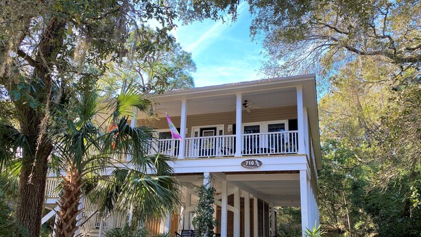 A two-story house with a covered porch, surrounded by trees and a well-maintained garden. - Dragonfly-Private Setting w/ Easy Beach Access; Covered & Screened Porch;TV/WiFi (Edisto Beach)