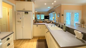 A modern kitchen with white cabinetry, a built-in refrigerator, a sink, and a dining area with a table and chairs. - Dragonfly-Private Setting w/ Easy Beach Access; Covered & Screened Porch;TV/WiFi (Edisto Beach)