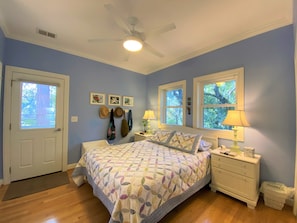 A bedroom with a bed, two windows, a ceiling fan, and a nightstand with lamps.