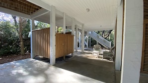 A covered porch with a wooden fence, a staircase, and two wicker chairs. - Dragonfly-Private Setting w/ Easy Beach Access; Covered & Screened Porch;TV/WiFi (Edisto Beach)