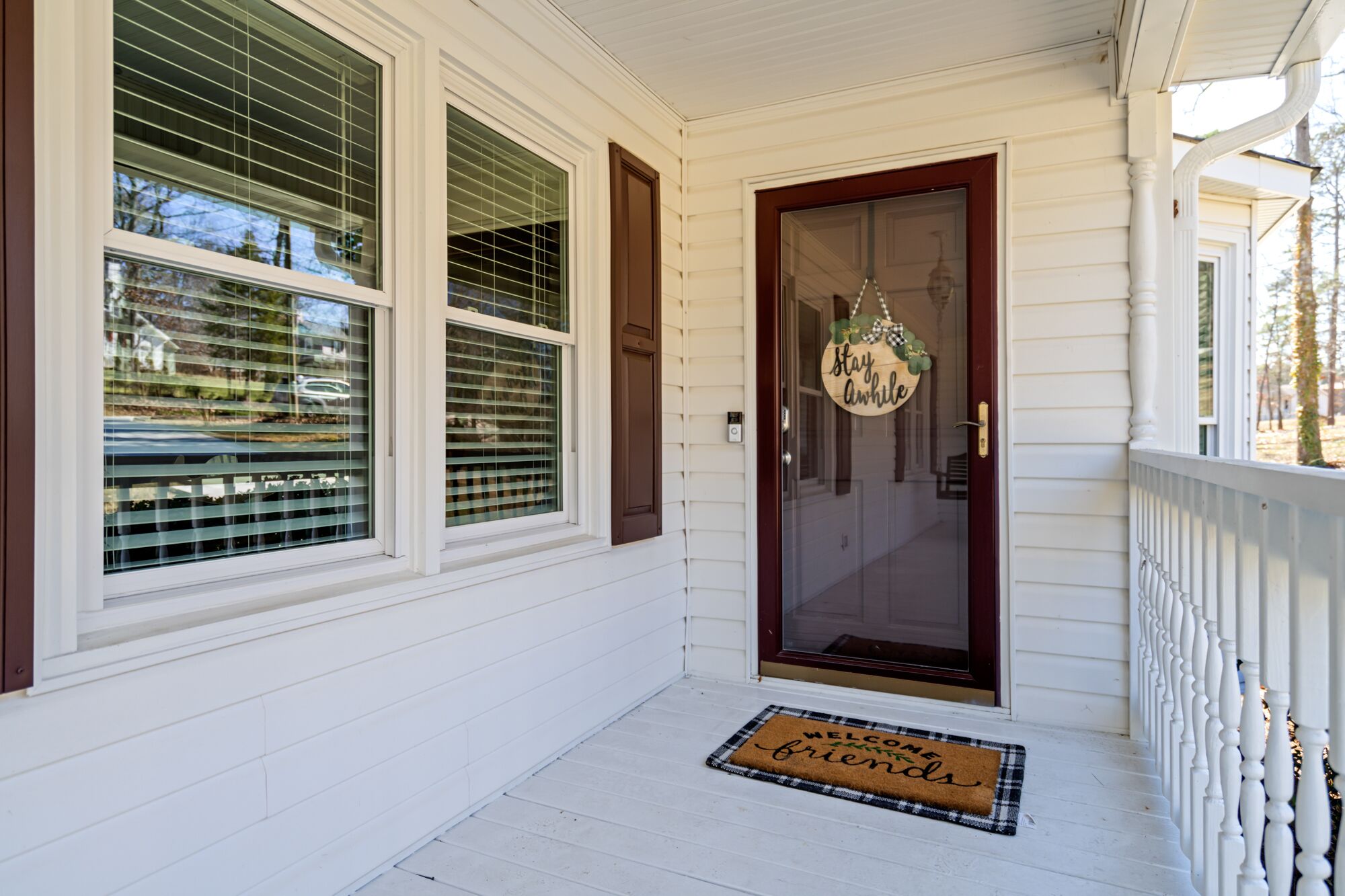 A white house with a front door, a welcome mat, and a sign that says "Stay awhile".