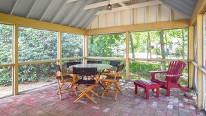 Un patio cubierto con suelo de ladrillo, ventanas amplias y mobiliario exterior que incluye una mesa y sillas.