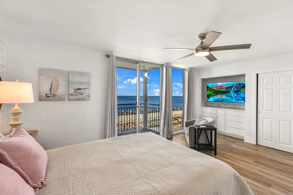Une chambre avec un lit, un ventilateur de plafond, une télévision et une vue sur l’océan, accessible par une porte-fenêtre coulissante.