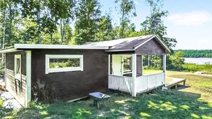 Eine kleine Holzhütte mit Veranda, einem Fenster und einer Schubkarre davor.