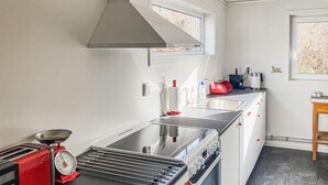 Eine kleine Küche mit einem Gasherd, einer roten Waage, einem Spülbecken und einem Fenster mit Blick auf Bäume.