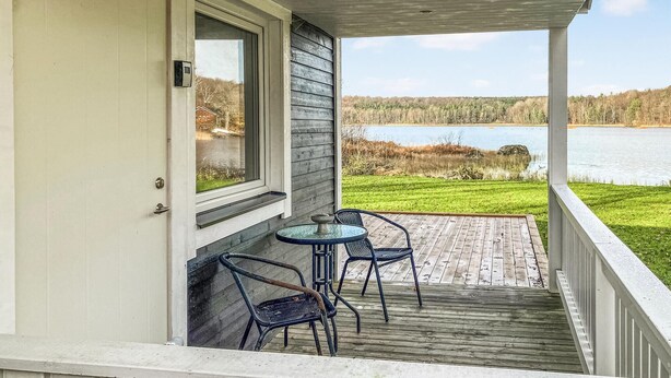 Überdachter Balkon mit zwei Stühlen und einem Tisch mit Blick auf einen See und eine Rasenfläche.