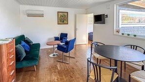 Ein Zimmer mit einem grünen Sofa, blauen Stühlen, einem runden Tisch und einem Fernseher an der Wand.