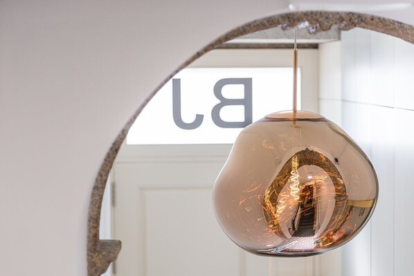 A pendant light with a reflective surface and visible filament inside, hanging from a curved metal structure.