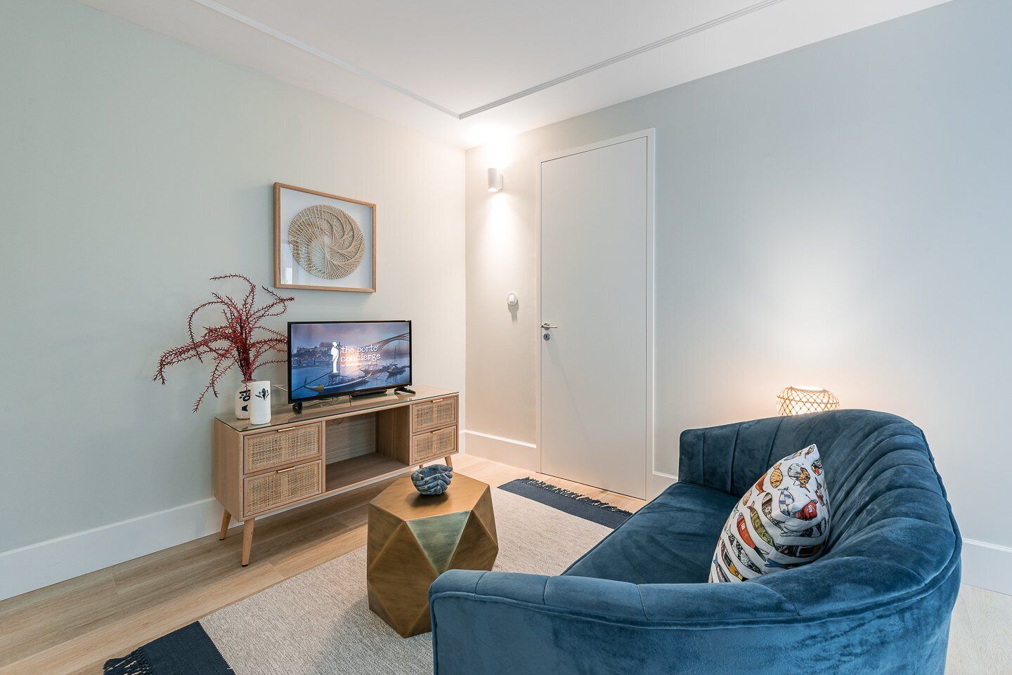 Un salon moderne avec un canapé bleu, un téléviseur posé sur une console en bois, un élément décoratif mural et une porte.