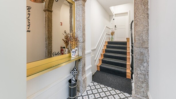 Eine Treppe mit schwarzen Teppichstufen, ein Glastischchen mit Dekoration und ein Spiegel mit goldener Rahmen.