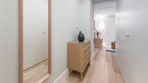 Ein Flur mit einem Holzschrank und einer großen Vase, der zu einem Raum mit einem Bett und einem Nachttisch führt.